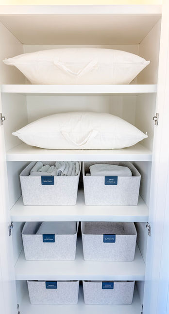 A luxury linen closet in Cherry Hills Village, CO with pillows on shelves stored in canvas linen bags, and towels and sheets on shelves below stored in Sort Joy felt bins. This closet was organized by KO Luxury Organizing.
