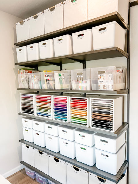 Craft supplies organized in white bins on grey floor to ceiling shelves