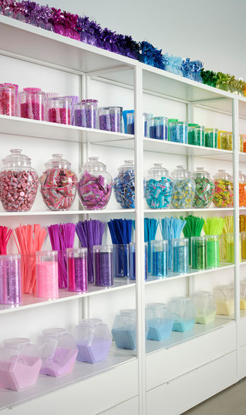 Crafts supplies organized by color in all kinds of fun storage bins on white IKEA shelves