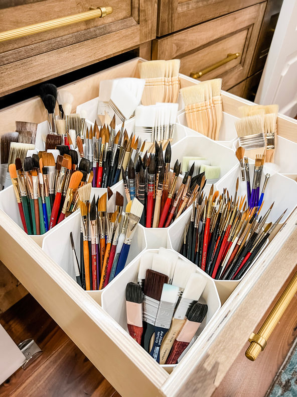 Paint brushes organized in a drawer in white bins