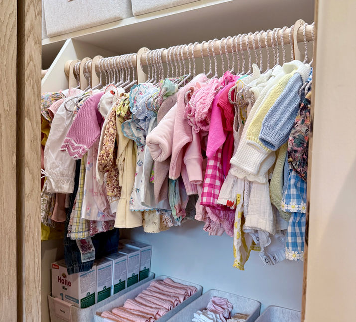 A nursery closet for a baby girl organized with soft felt baskets that have light pink labels and tiny dresses hanging on the rod with hang tags separating sizes - done by KO Luxury Organizing in Snowmass, CO.