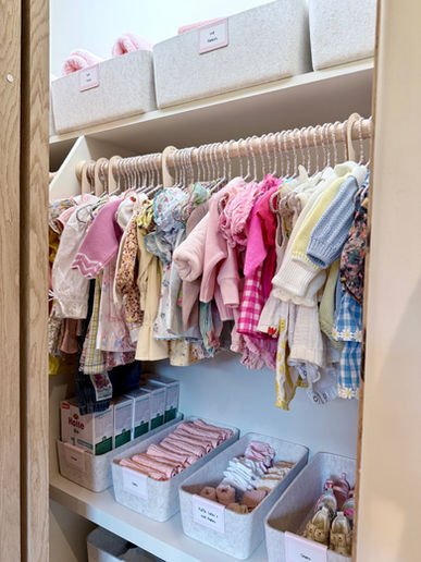 A nursery closet with baby clothes hanging and organized by age. Everything is pink and colorful!