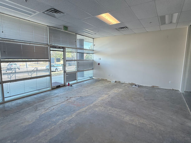 Empty reception area with unfinished concrete flooring, exposed walls, dated ceiling grid and lighting, and minimal visual identity prior to renovation.