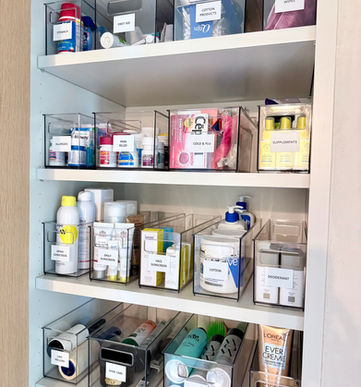 A beautifully organized medicine closet with everything organized in clear bins with white labels.