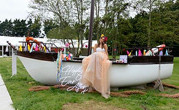 Bride sitting on the boat bar at Crown hall Farm, surrounded by colourful by colourful decorations during a festival wedding