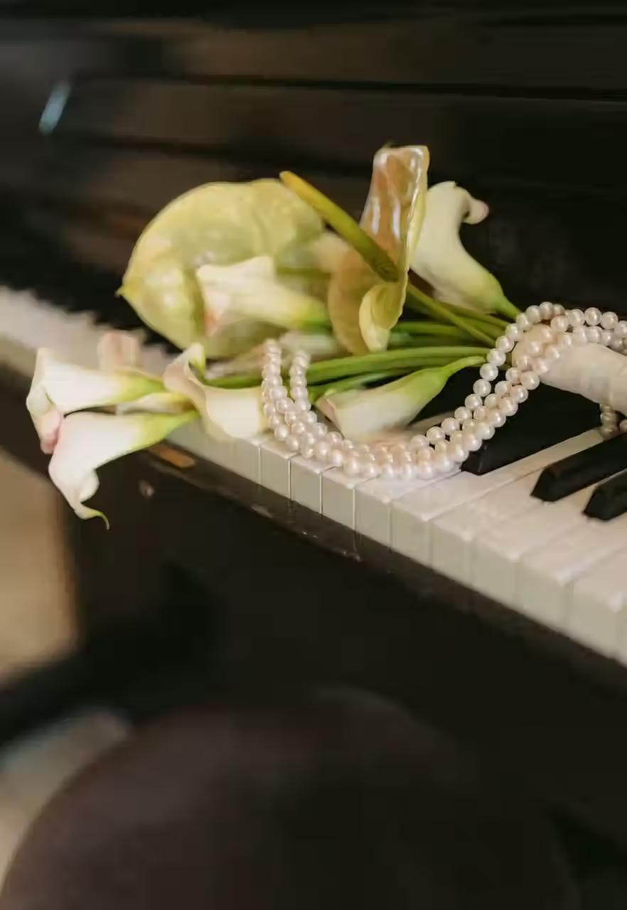 Composition florale avec arums et collier de perles posés sur un piano