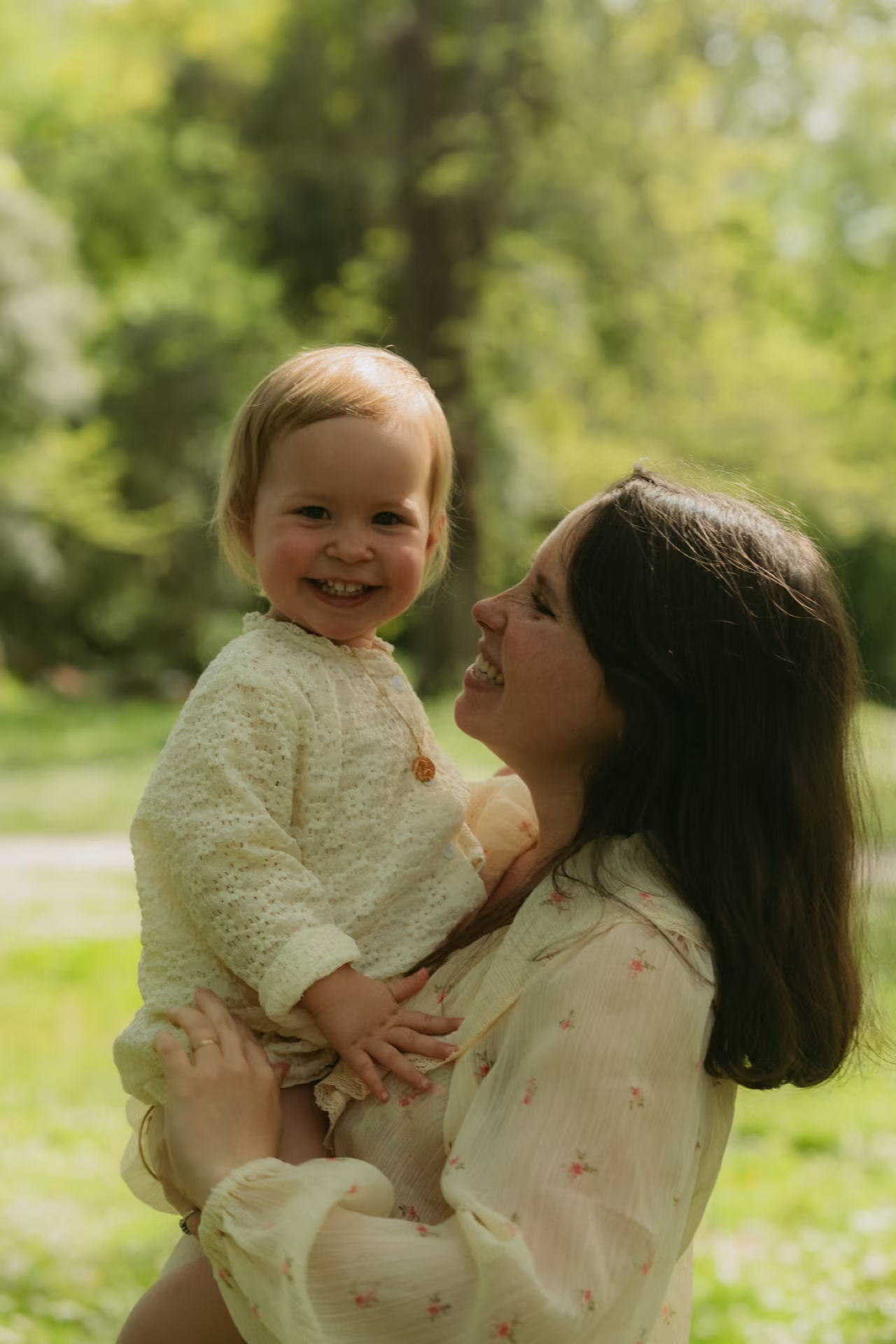 Maman portant sa petite fille souriante lors d'une séance famille dans le parc de Majolan à Blanquefort