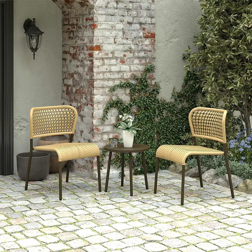 Outdoor patio setup with two rattan chairs and a black table on stone paving, placed against a white brick wall with greenery