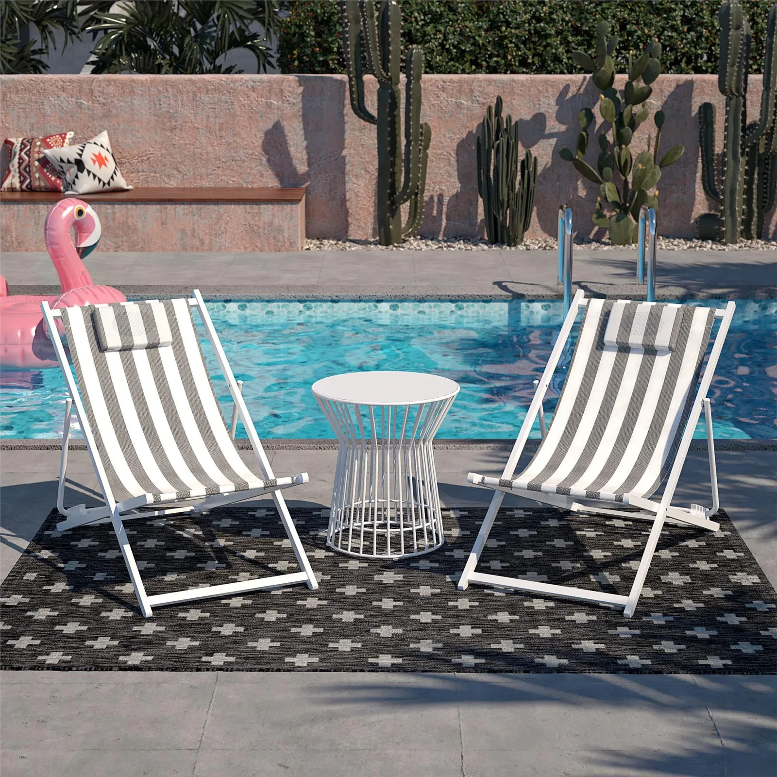 Striped lounge chairs by a pool with a small round table between them and a pink inflatable flamingo in background.