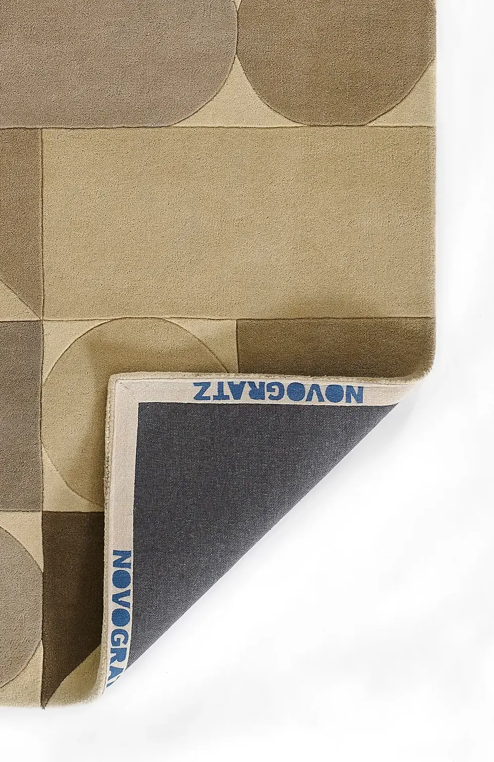 Close-up of a taupe area rug with geometric shapes in muted tones, showing the folded corner to reveal the backing.