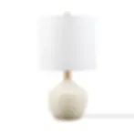 Table lamp with a cream ceramic base and a cylindrical white fabric shade, featuring a gold neck and finial.