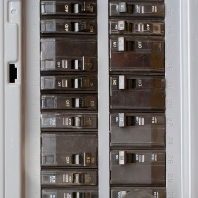 Close-up of an electrical breaker panel with multiple black switches labeled ON and OFF in a gray enclosure. Neutral lighting.