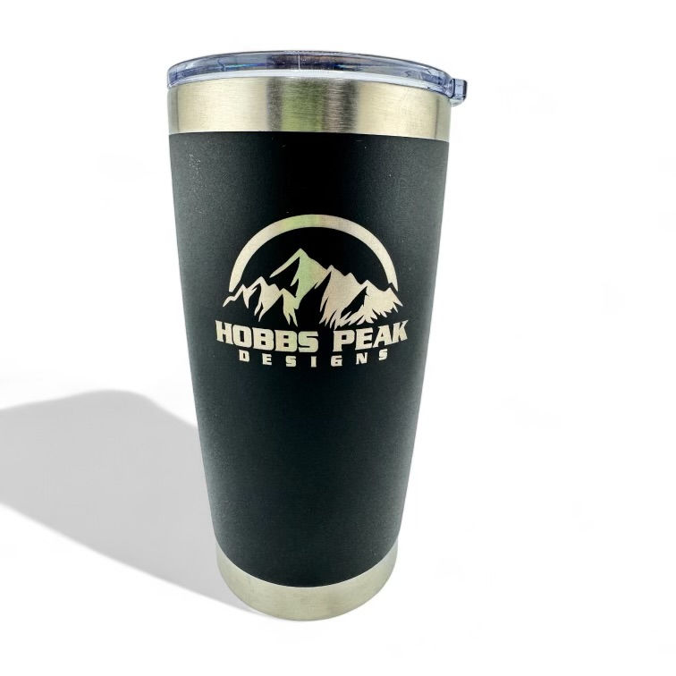 "The image shows a black tumbler with a silver rim and a clear lid. The tumbler has a logo on it that features a mountain range with the text 'HOBBS PEAK DESIGNS' written below the mountains. The logo and text are in a light color, contrasting with the dark background of the tumbler. The tumbler appears to be made of stainless steel and is designed for keeping beverages hot or cold.