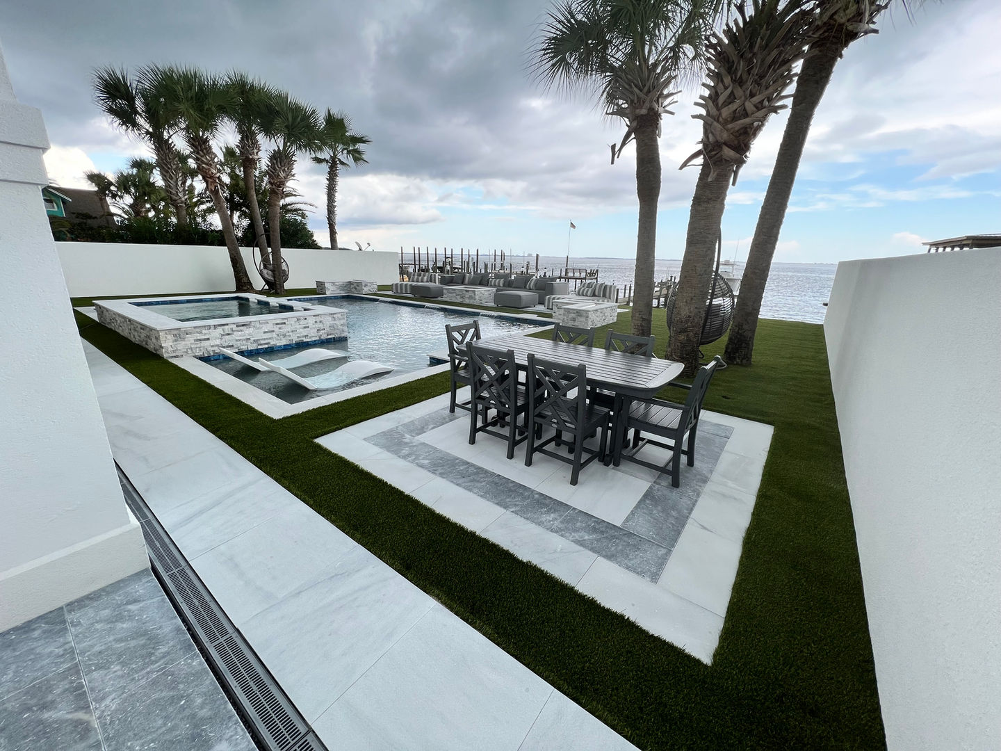 Luxury waterfront backyard with custom pool, artificial turf installation, gas fire pits, and modern outdoor living design by Turf Tailors in Fort Walton Beach, Florida. Destin pavers palm trees
