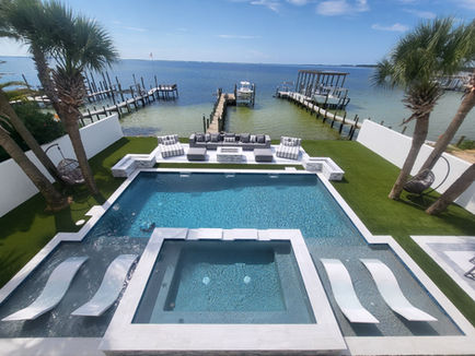 Luxury waterfront backyard with custom pool, artificial turf installation, gas fire pits, and modern outdoor living design by Turf Tailors in Fort Walton Beach, Florida. Destin pavers palm trees