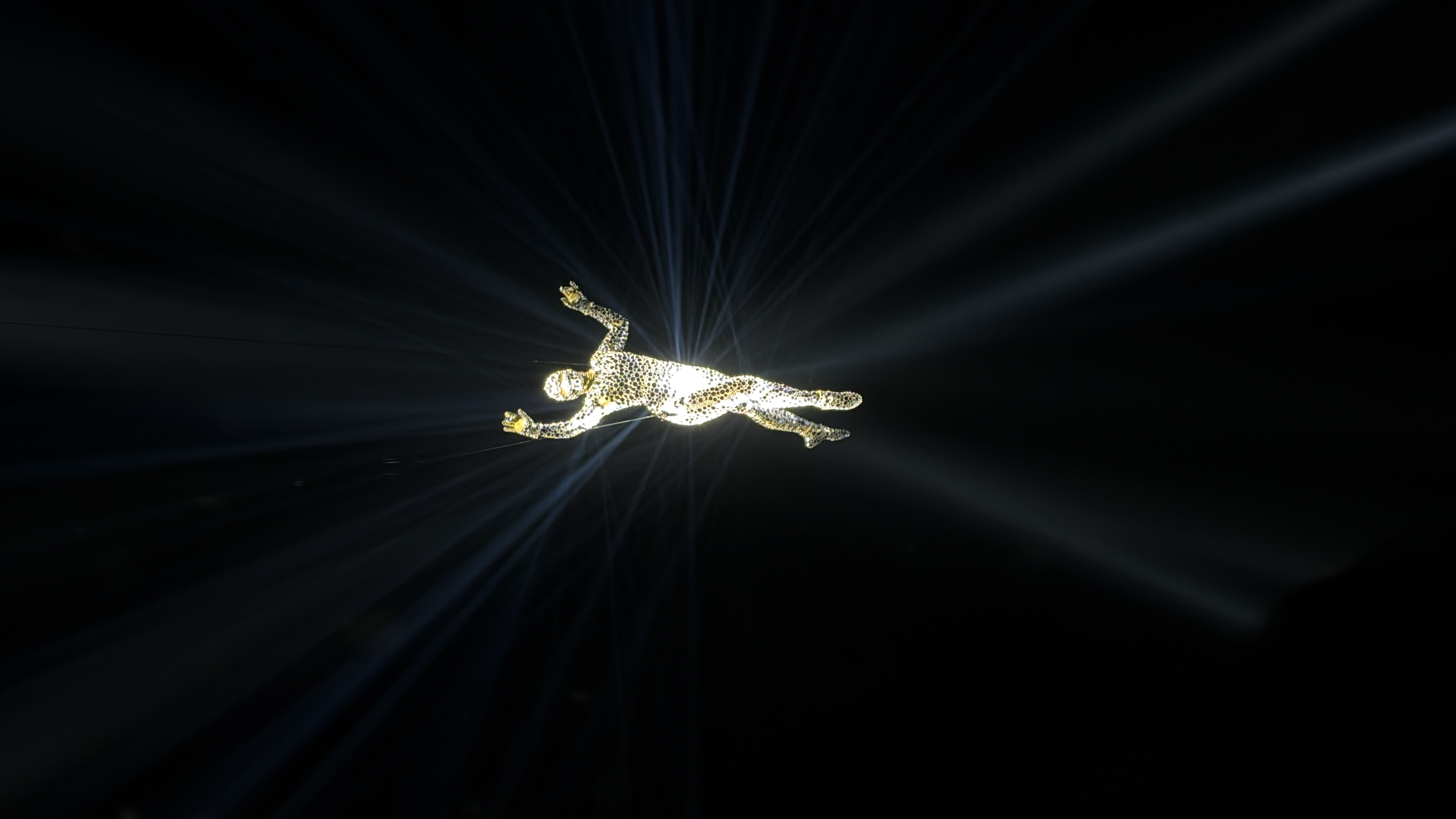 An illuminated human-shaped figure with raised arms radiates beams of light against a dark background.
