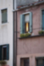 Window with open shutters and light shining from inside, with a plant box below from the Canals in Venice, Italy