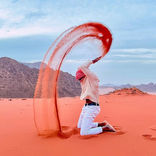 Il creatore di contenuti di viaggi di lusso Sammy Vagabond è seduto in ginocchio e lancia sabbia rossa in aria nel deserto del Wadi Rum in Giordania