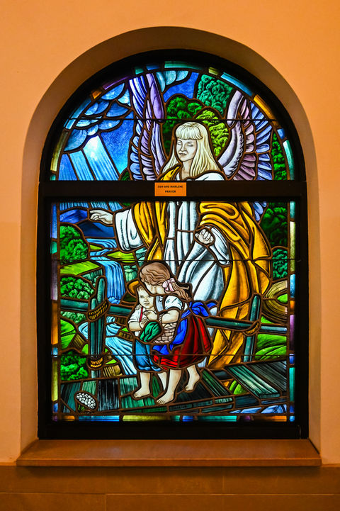 Stained glass of angel guiding child over bridge
