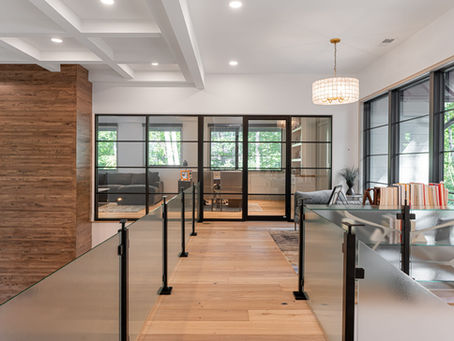Light wide-plank hardwood flooring running through an open hallway with glass railings and black-framed windows.