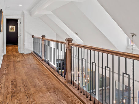 Warm-toned hardwood flooring beside a coordinated wood handrail and black metal balusters on an upstairs landing.