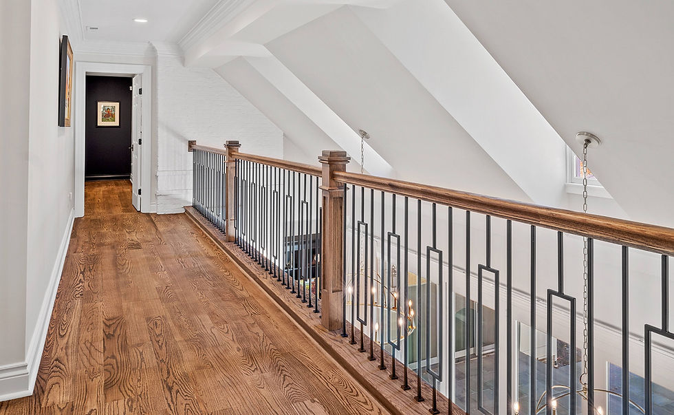 Warm-toned hardwood flooring beside a coordinated wood handrail and black metal balusters on an upstairs landing.
