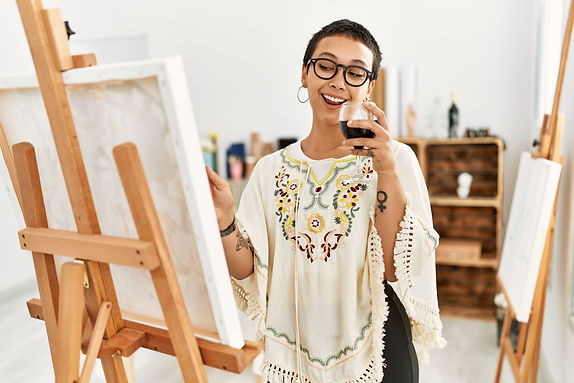 A young woman drinks wine while painting on a canvas..jpg