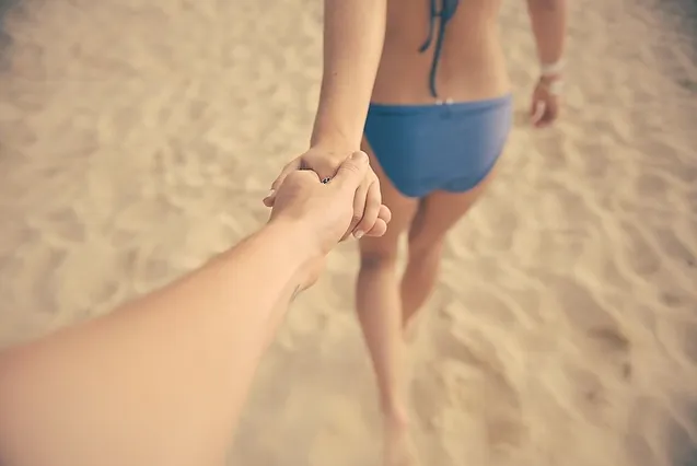 Sigueme. Pareja en la playa cogidos de la mano Mujer tirando de la mano de su pareja en la playa