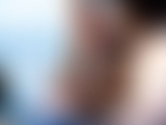 Two colleagues discuss a document on a tablet in an office with blue curtains, a laptop, and papers on the table, in soft light.