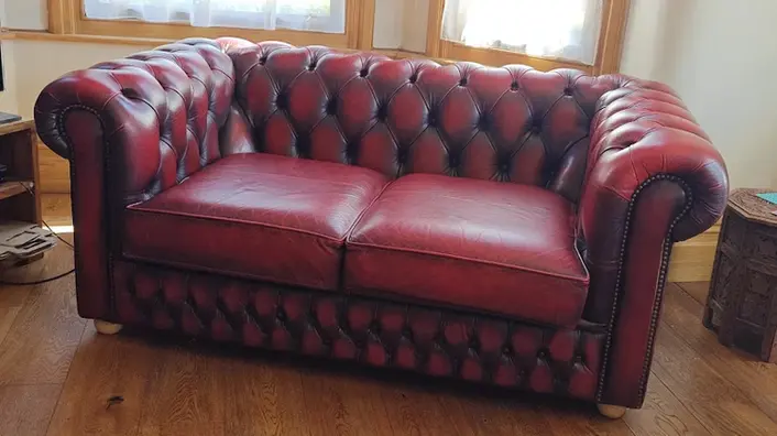 Two-seater Chesterfield sofa in oxblood red leather with deep button tufting and rolled arms, professionally restored by A2Z Upholstery in Manchester