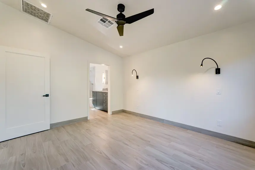 Interior guest house bedroom with view of bathroom entrance, reading light fixtures, and ceiling fan