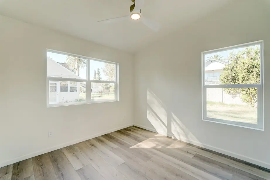 Empty ADU bedroom with vaulted ceiling, recessed lighting, large window, and light wood-look flooring.