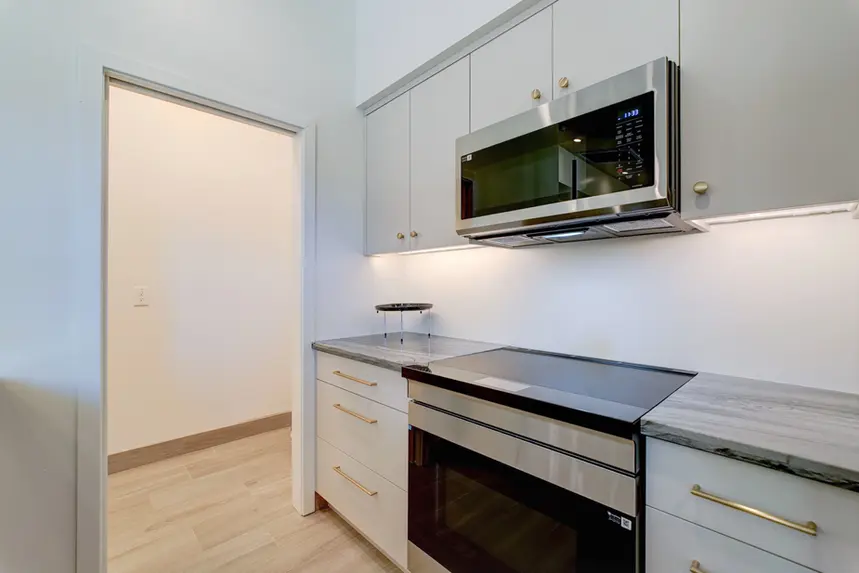 Interior guest house kitchen view with range oven and microwave, gray countertops, and view of pantry