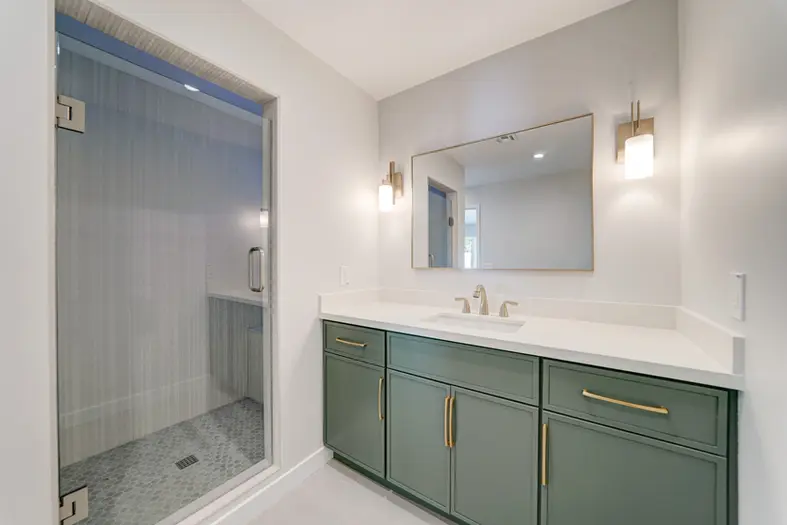 Modern ADU bathroom featuring a green vanity, gold hardware, and a glass-enclosed walk-in shower.