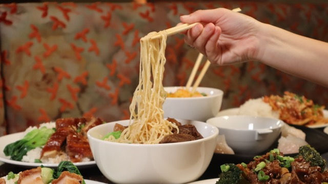 A portion of springy wheat noodles being lifted from a steaming bowl of traditional soup at Good Friends.