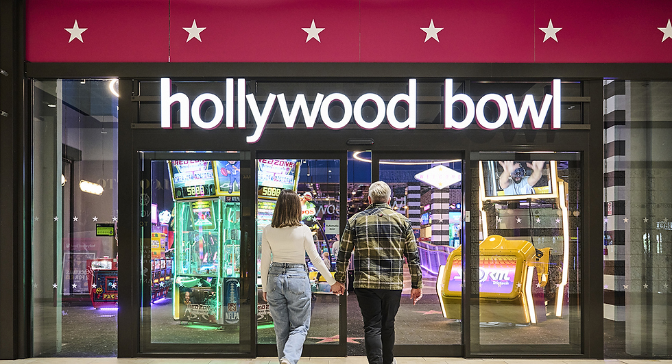 Couple holding hands enters Hollywood Bowl arcade entrance, with neon game machines glowing inside.