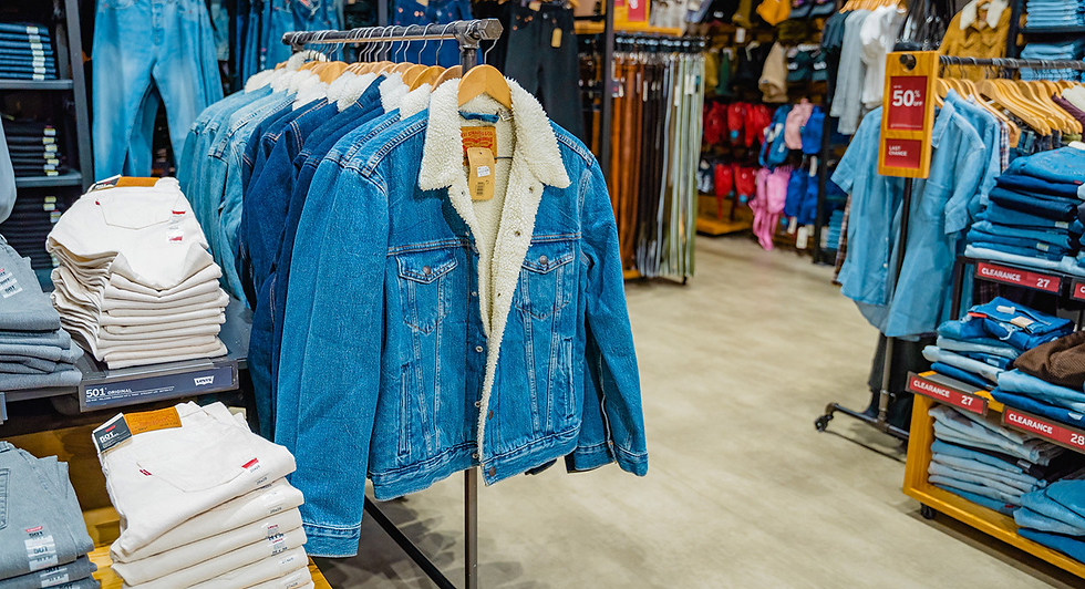 Denim jacket with white shearling collar hangs in a clothing store aisle, surrounded by folded jeans and red clearance signs. - levi's outlet from resorts world birmingham