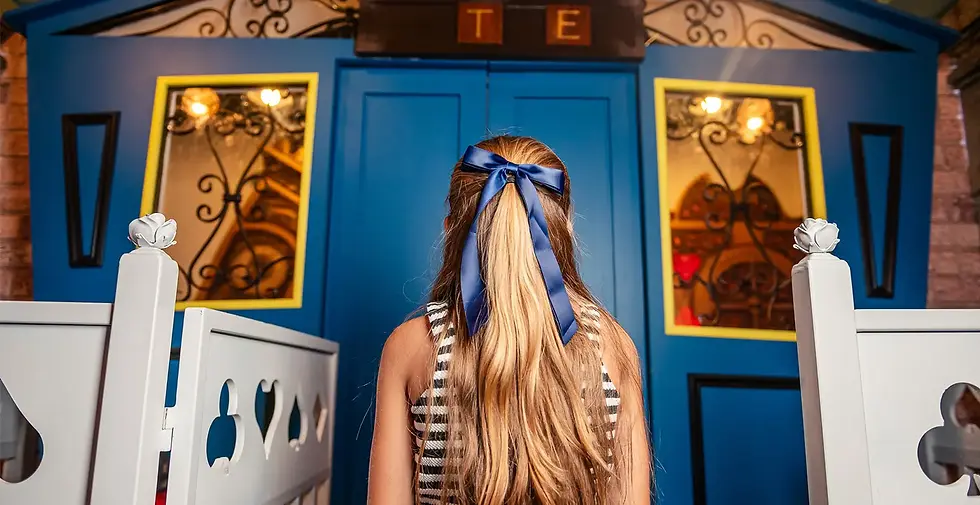 Girl with long hair and blue ribbon stands at a blue entrance with white gates and TE sign.