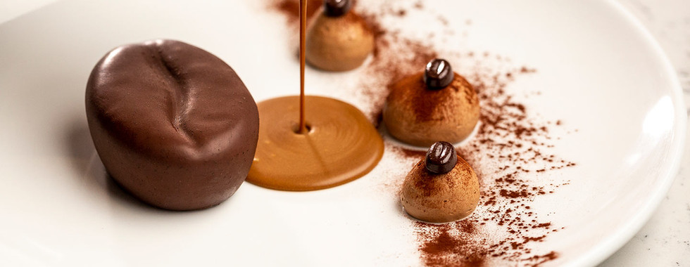 A decadent coffee-bean-shaped chocolate mousse being drizzled with warm, silky chocolate ganache for a gourmet dessert.