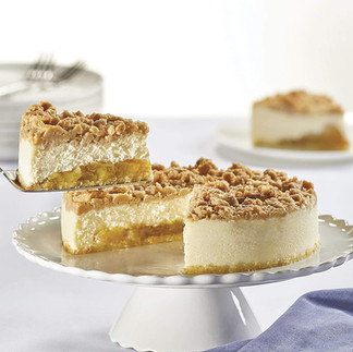 A slice of Junior’s apple crumb cheesecake being lifted from a whole cake on a white ceramic pedestal stand.