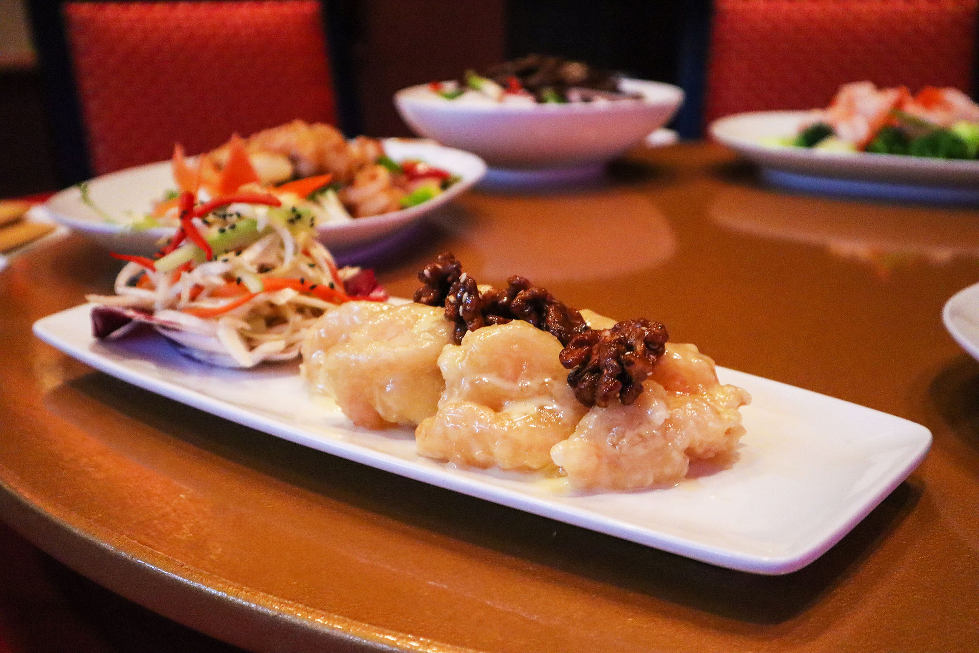 Signature honey walnut shrimp served with a side of fresh vegetable salad on a long white platter at Lotus.