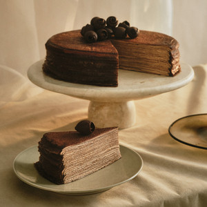 Decadent Lady M Chocolate Mille Crêpes cake with thin layers of handmade crêpes and cocoa cream on a marble cake stand.