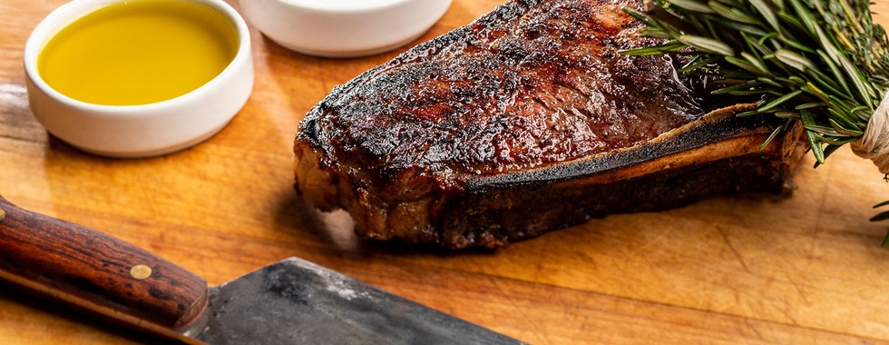 A perfectly seared bone-in ribeye steak resting on a wooden carving board with fresh rosemary and a professional chef's knife.