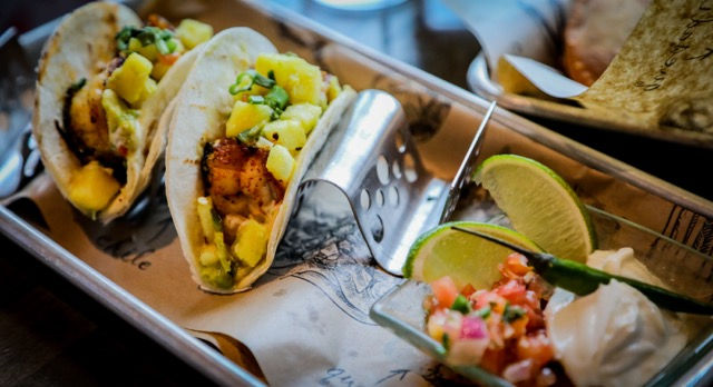 Close-up of a gourmet shrimp taco topped with pineapple salsa and fresh lime at Dos Gatos.