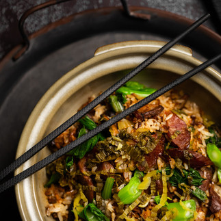 Close-up of traditional claypot rice with Chinese sausage (lap cheong) and green vegetables in an earthenware pot.