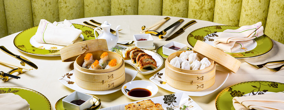 A luxury dim sum spread featuring bamboo steamers, radish cakes, and artisanal dumplings on a formal green and gold table setting.