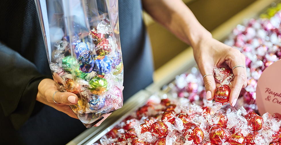 Hands fill a clear bag with colorful Lindor chocolates from a candy shop display bin. - lindt resorts world birmingham