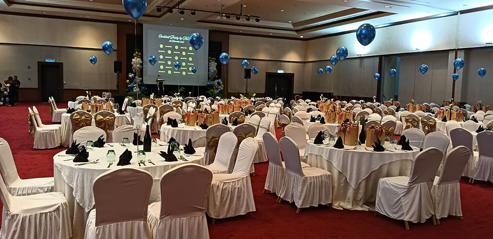 Decorated banquet hall with round tables, white chair covers, blue balloons, and a stage screen for a celebration.