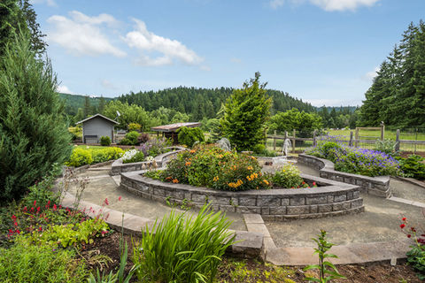 Tiered circular garden with stone walls, lush trees, and blue sky.