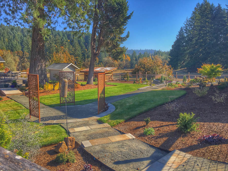 Paved path through decorative gates entering a lush garden with autumn trees.